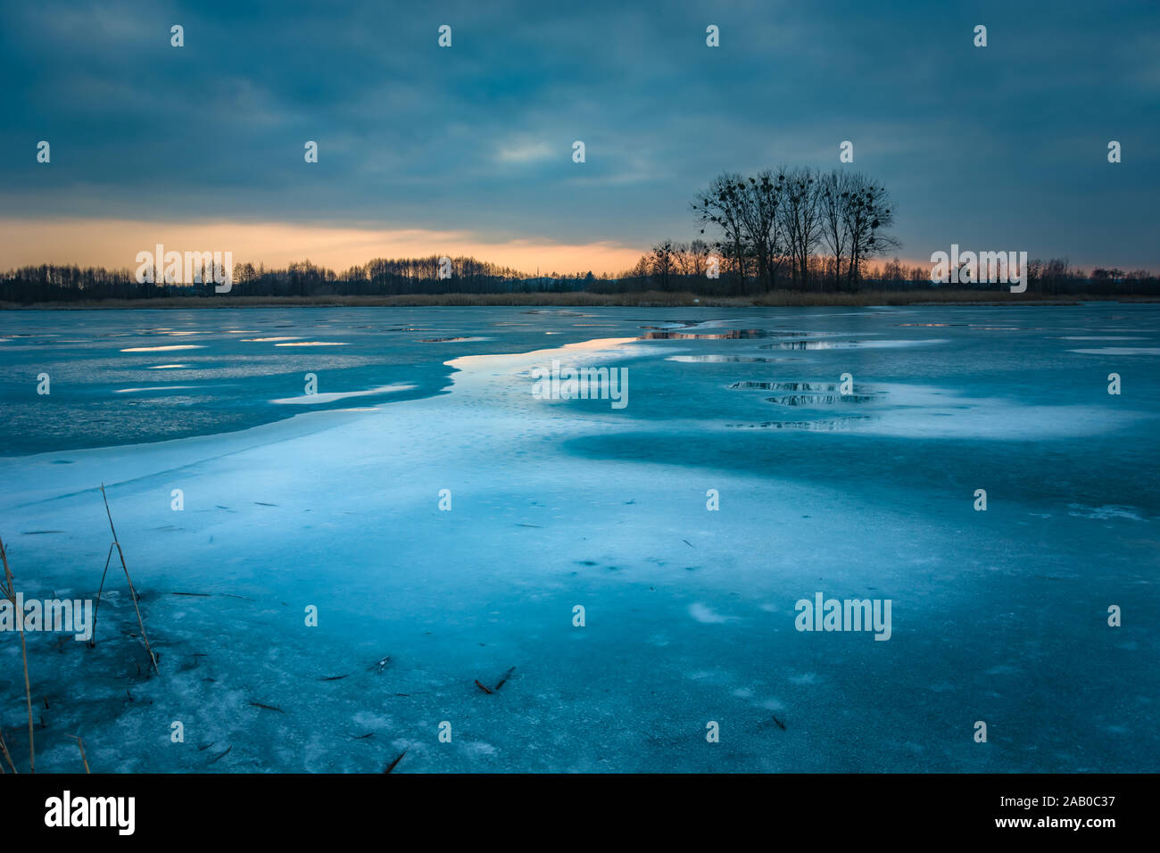 Eis auf einem zugefrorenen See, Bäume am Horizont und den Abendhimmel nach Sonnenuntergang, im östlichen Polen Stockfoto