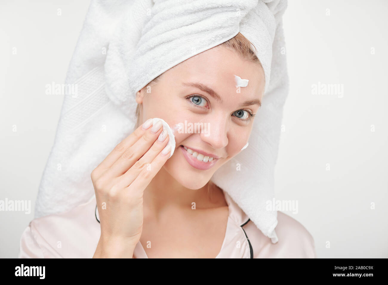 Hübsche junge gesunde Frau mit Baumwolle Pad für die Anwendung feuchtigkeitsspendende Creme im Gesicht Stockfoto