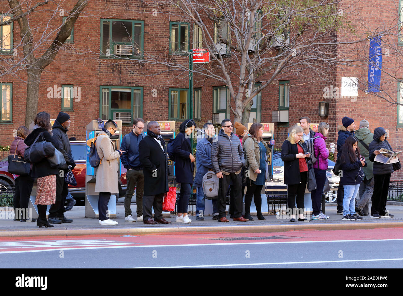 Menschen, die an einer Bushaltestelle auf der East Side von Manhattan am Ende der morgendlichen Hauptverkehrszeit warten, New York, NY (21. November 2019) Stockfoto