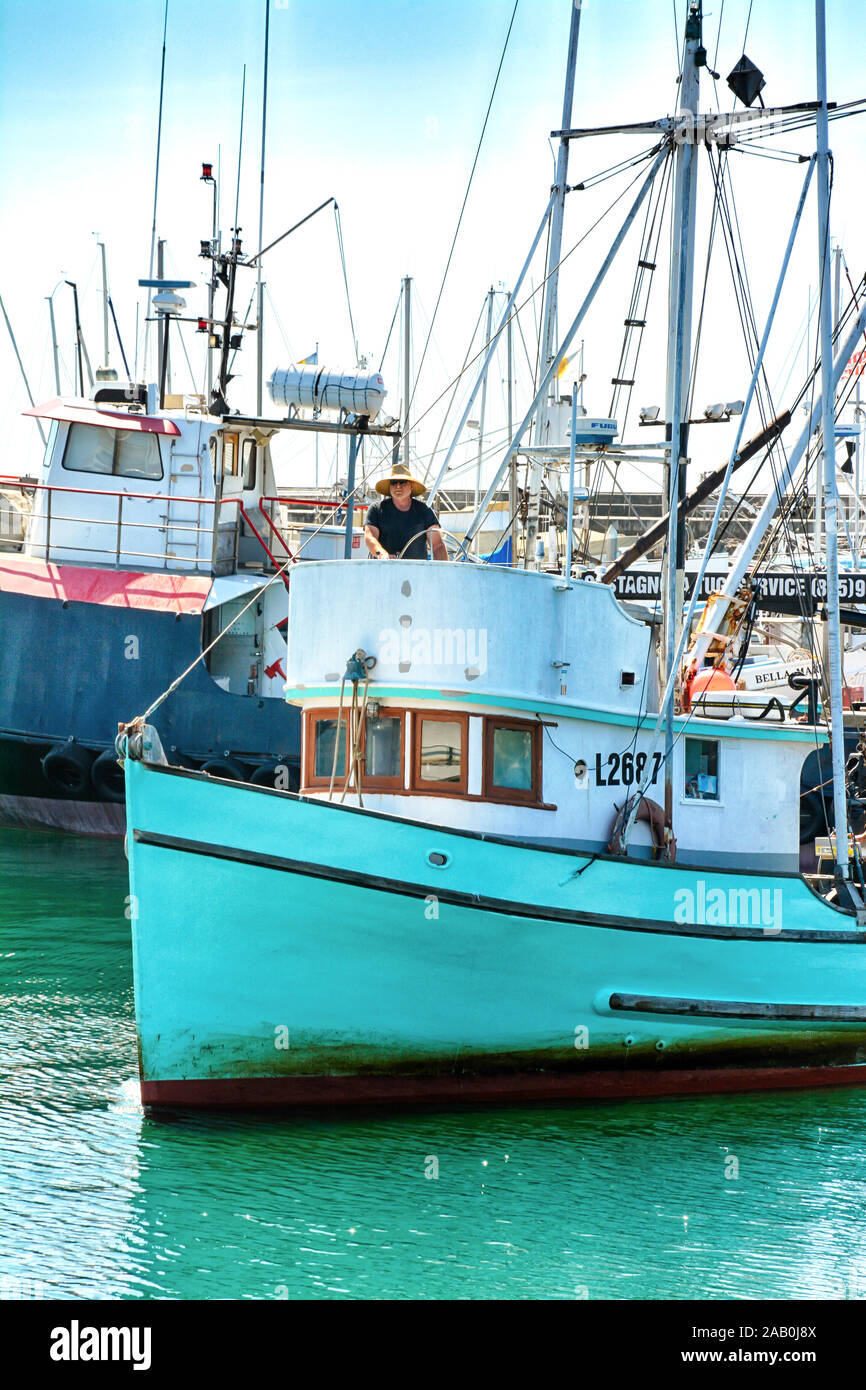 Ein zwangloser Kapitän manövriert ein kommerzielles Fischerboot, während er von den Docks der Marina im Santa Barbara Hafen in Südkalifornien startet Stockfoto