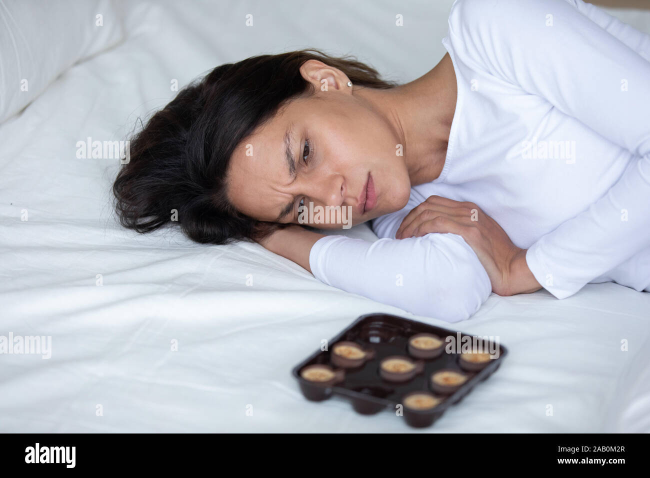 Depressiven Frau liegend auf Bett in der Nähe Schokolade Süßigkeiten fühlt sich einsam Stockfoto