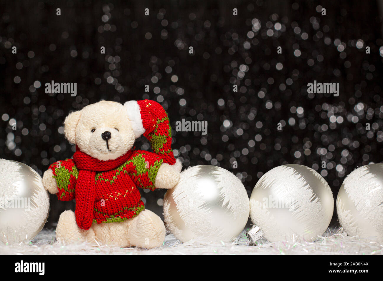 Weihnachten Ansicht der Teddybär in rot grünen Pullover und Mütze und die vier silbernen Abend Kugeln mit weißem Schnee auf es auf dunklem Hintergrund mit Silber Stockfoto