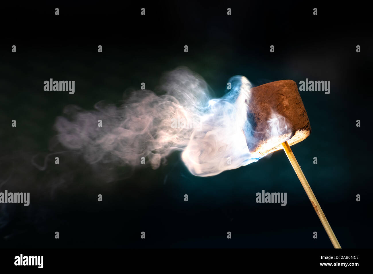 Die Röstung Schokolade überzogen Marshmallow auf einem Stick; Rauch wirbelt auf einem dunklen Hintergrund sichtbar Stockfoto