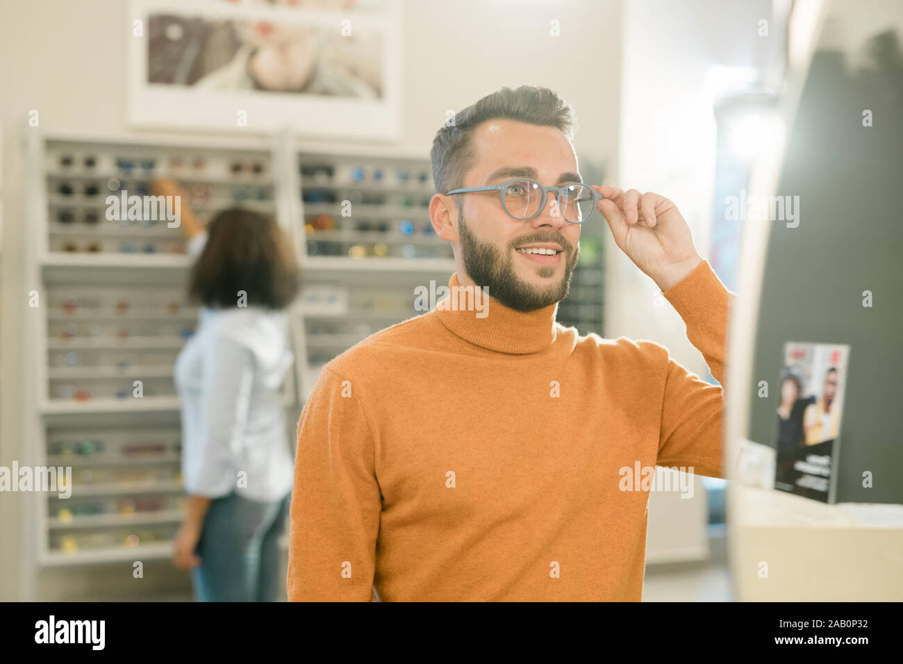 Junge lächelnde Mann in Pullover versuchen, auf neue Brillen vor Spiegel Stockfoto