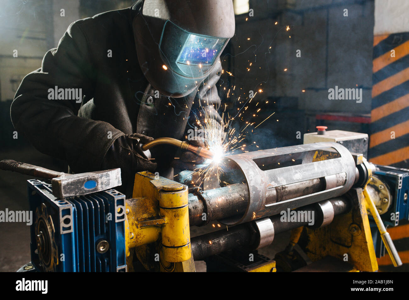 Schweißer bei der Arbeit abgedeckt. Er ist Schweißen metall Stück, mit industriellen Schelle befestigt. Stockfoto