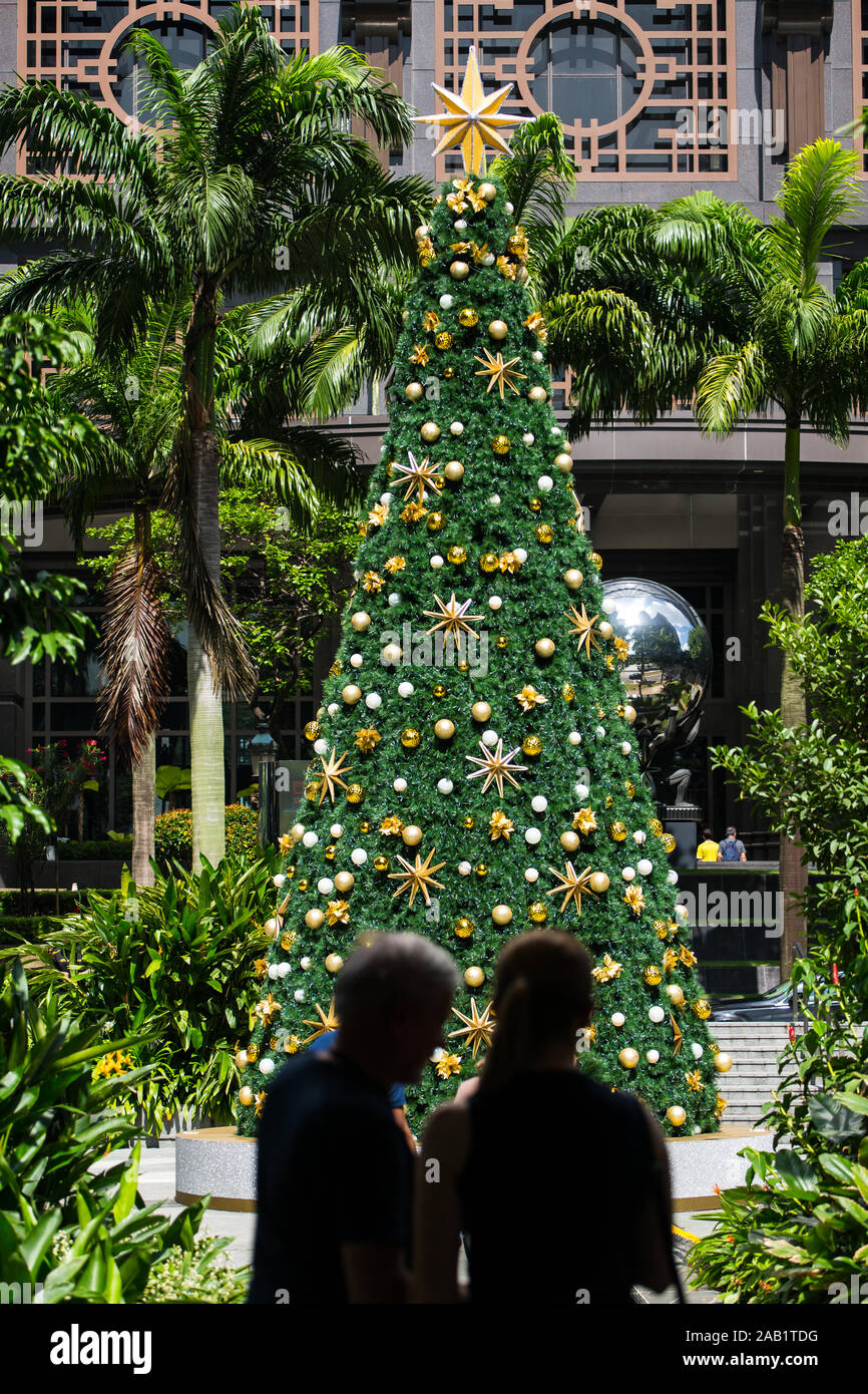 Vertikale Ansicht von zwei Personen in Silhouette, die vor einem hohen Weihnachtsbaum mit einem goldenen Stern an der Spitze stehen, Singapur, Südostasien. Stockfoto