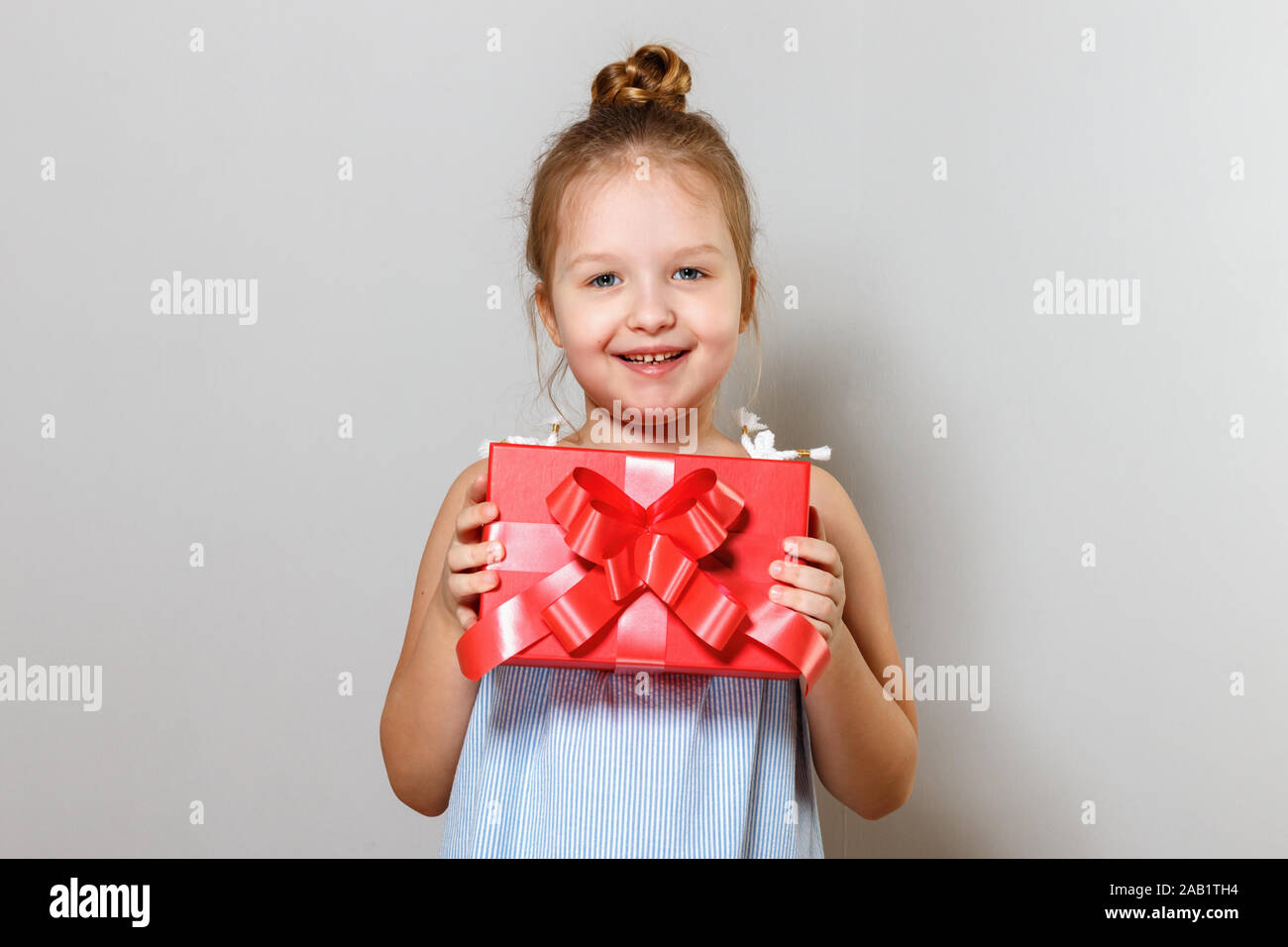 Closeup Portrait von ein süßes kleines Mädchen mit einer Geschenkbox. Baby auf grauem Hintergrund. Stockfoto