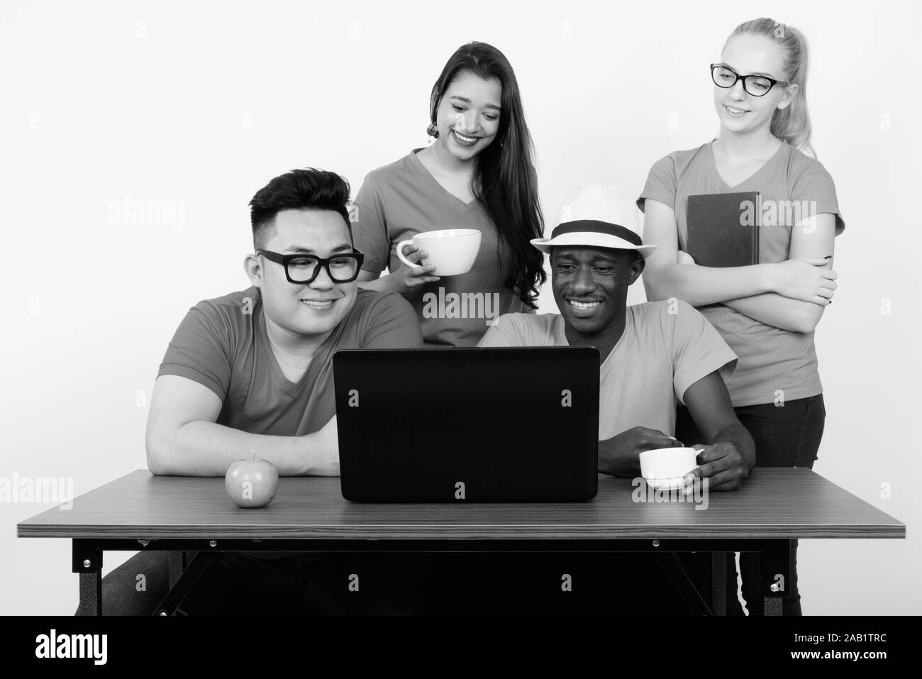 Gerne vielfältige Gruppe von multi-ethnische Freunde lächelnd und mit Laptop während Kaffee mit grünem Apfel auf hölzernen Tisch Stockfoto