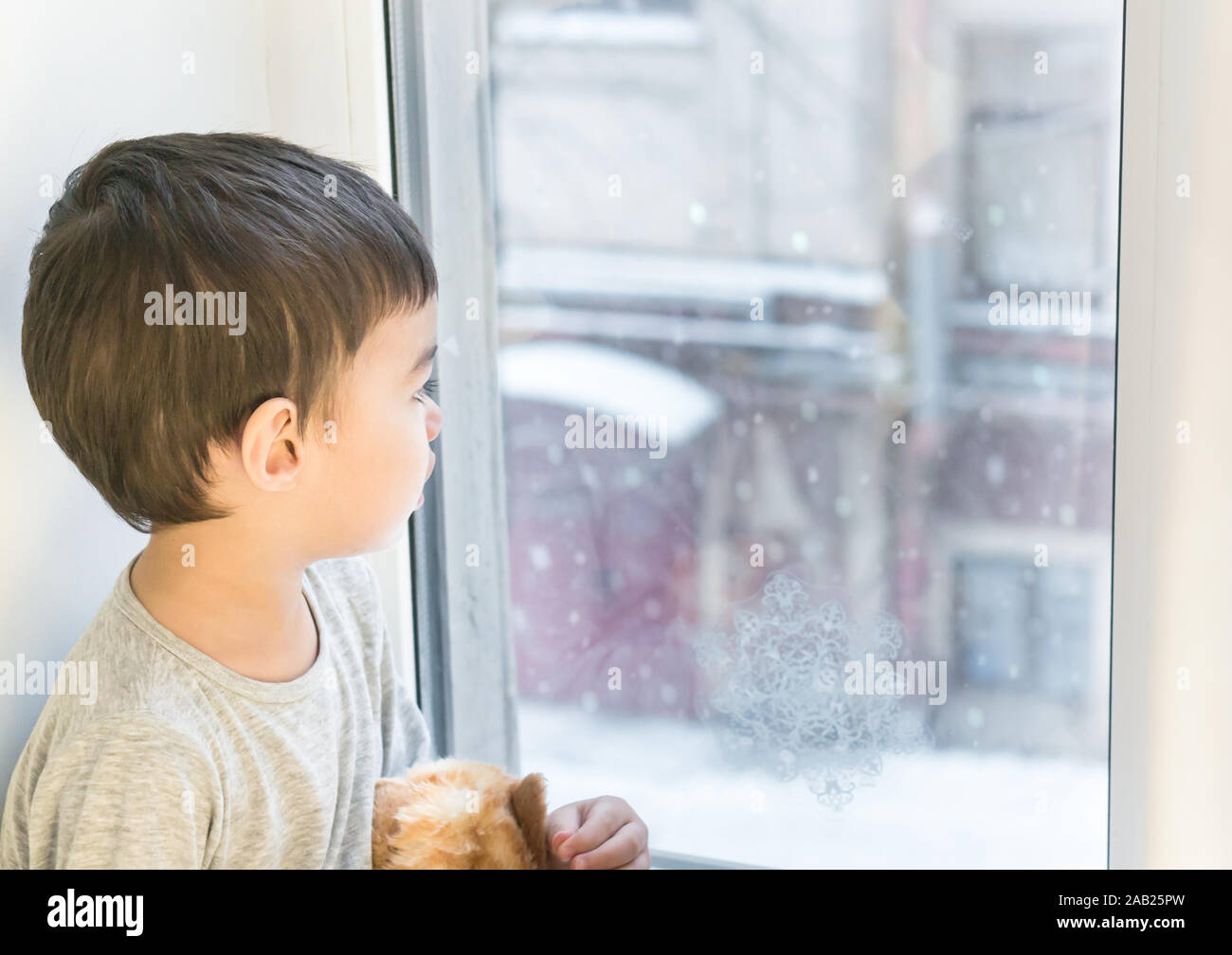 Kleiner Junge Blick durch das Fenster, gerade Schnee im Winter Stockfoto