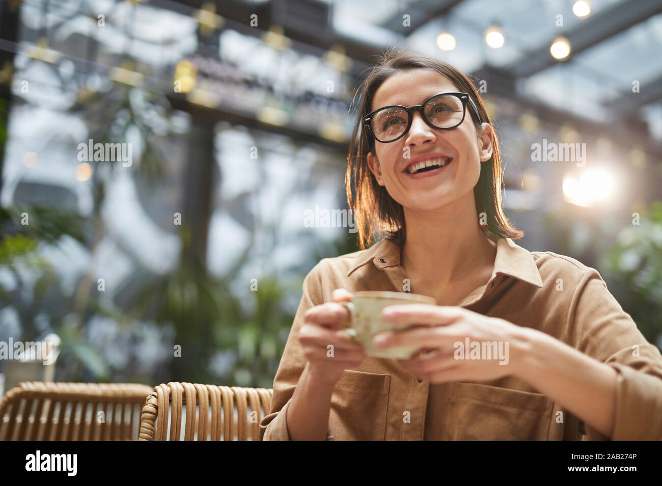 Low Angle Portrait von fröhliche junge Frau mit Tasse Kaffee im Cafe sitzen im Freien Terrasse, Kopie Raum Stockfoto