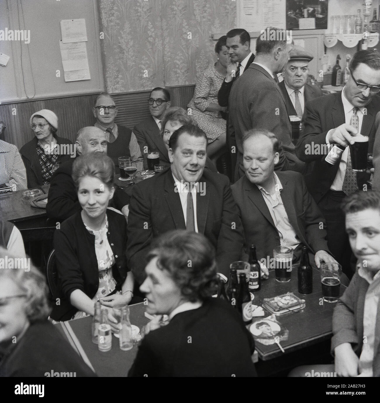 In den 1960er Jahren sitzen historische Männer und Frauen an Tischen mit Getränken und genießen einen Abend in einem Working Men's Club, England, Großbritannien. Stockfoto