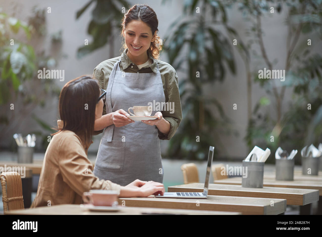 Portrait von lächelnden jungen Kellnerin Kaffee holen zu Client der Outdoor Cafe Terrasse mit Pflanzen dekoriert, kopieren Raum Stockfoto
