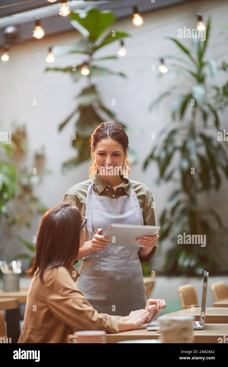 Portrait von lächelnden jungen Kellnerin Holding digital tablet, während die Bestellungen der Outdoor Cafe Terrasse beleuchtet durch warmes Sonnenlicht Stockfoto