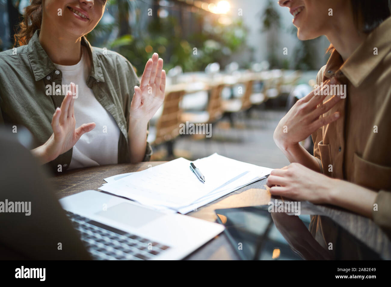 Nahaufnahme des unkenntlich junge Frau aktiv gestikuliert während der Sitzung im Cafe mit weiblichen Partner über Tabelle, kopieren Raum Stockfoto