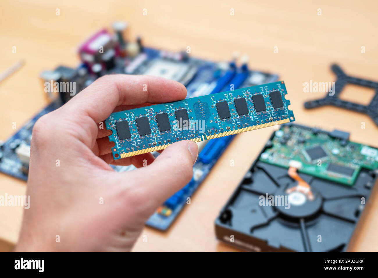 RAM-Speichermodul in der Hand. Mainboard und Festplatte im Hintergrund. Konzept der Installation. Stockfoto