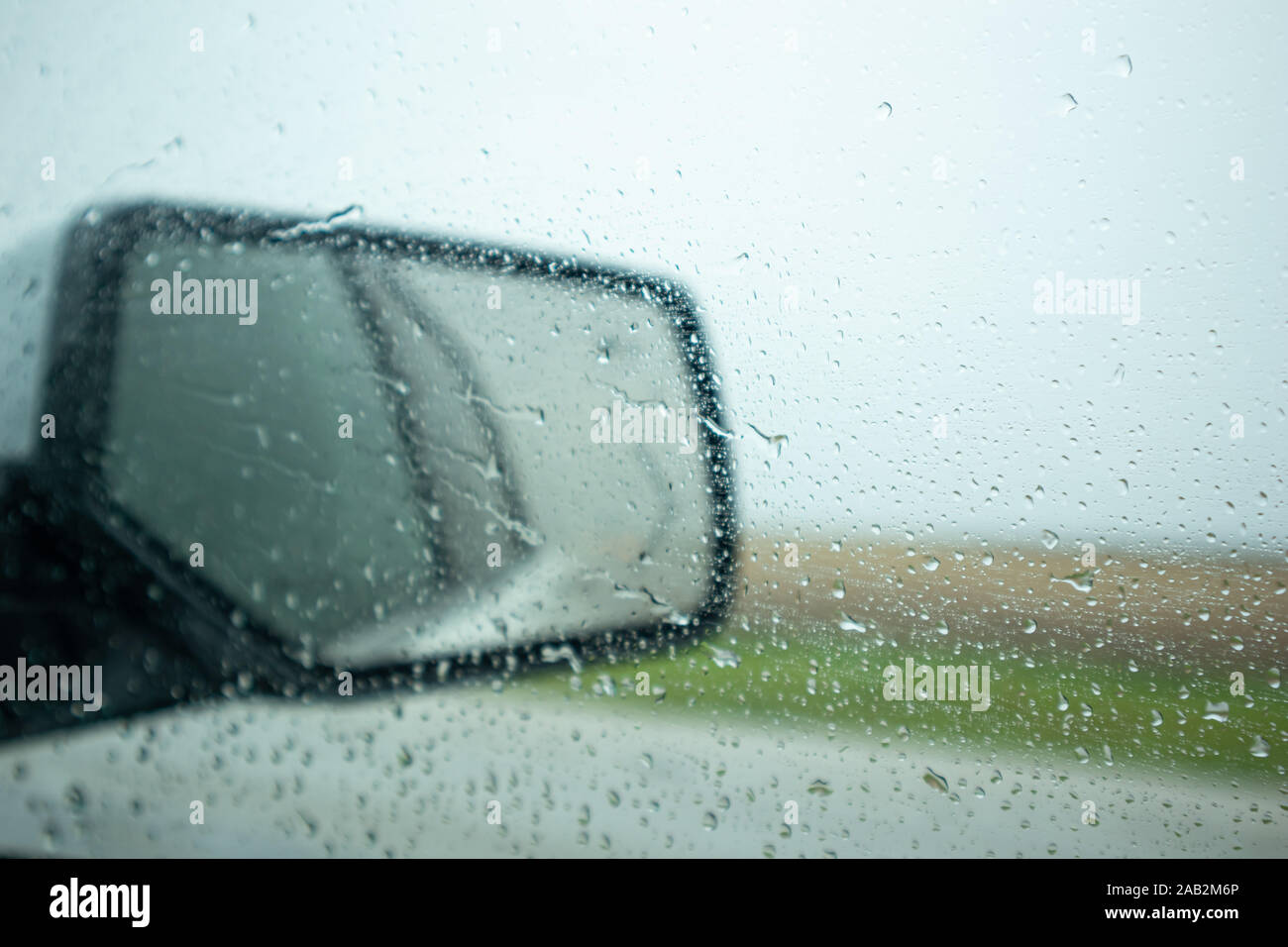 Fahrt auf der Autobahn einen regnerischen Frühlingstag. Regentropfen auf dem Fenster und am Kotflügel Spiegel, bewölkter Himmel, blur Landschaft Stockfoto