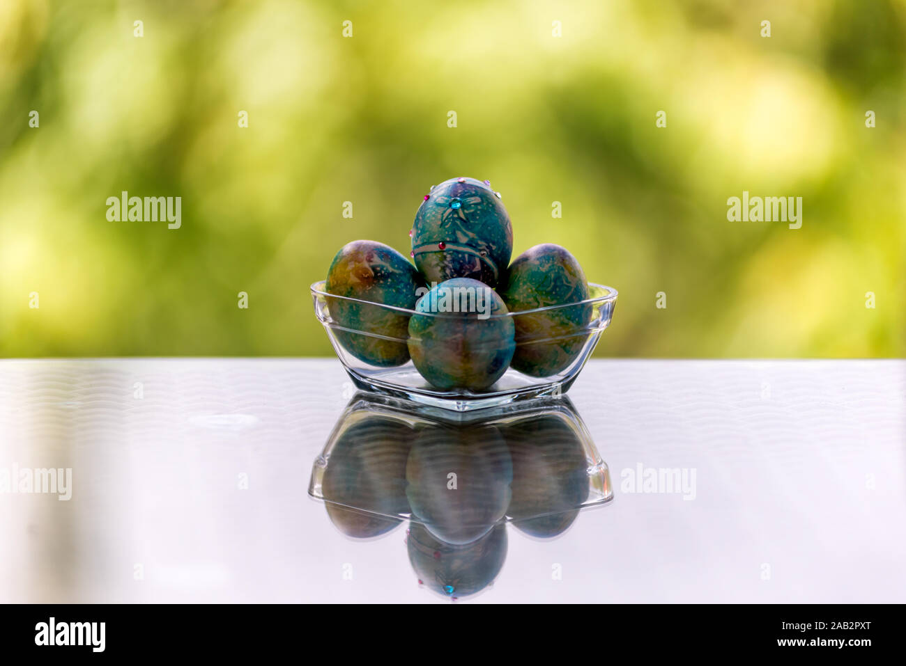 Ostern Dekoration - Blau, bunt bemalte Eier mit Edelsteinen in eine Glasschüssel auf einem Glastisch Stockfoto