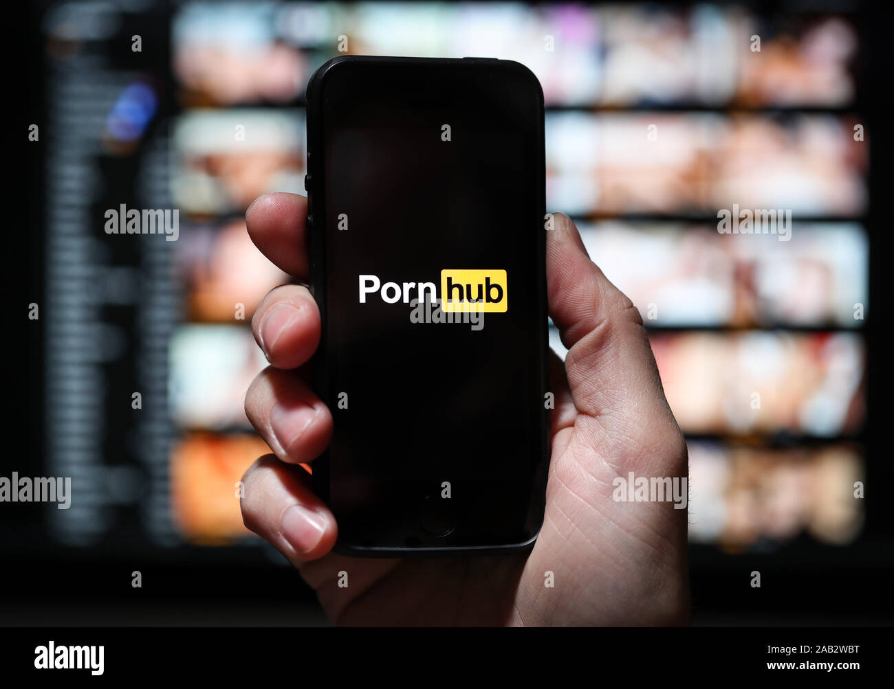 Ein Mann am Pornhub.com website Logo suchen auf seinem Telefon mit dem Pornhub Website auf einem Computer aus dem Fokus in den Hintergrund. Stockfoto