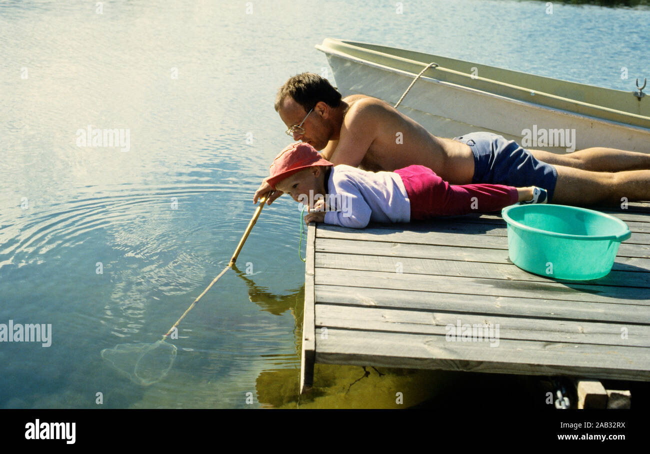 Vater und Kind liegen auf dem Dock mit Netzen und fangen Fische Stockfoto