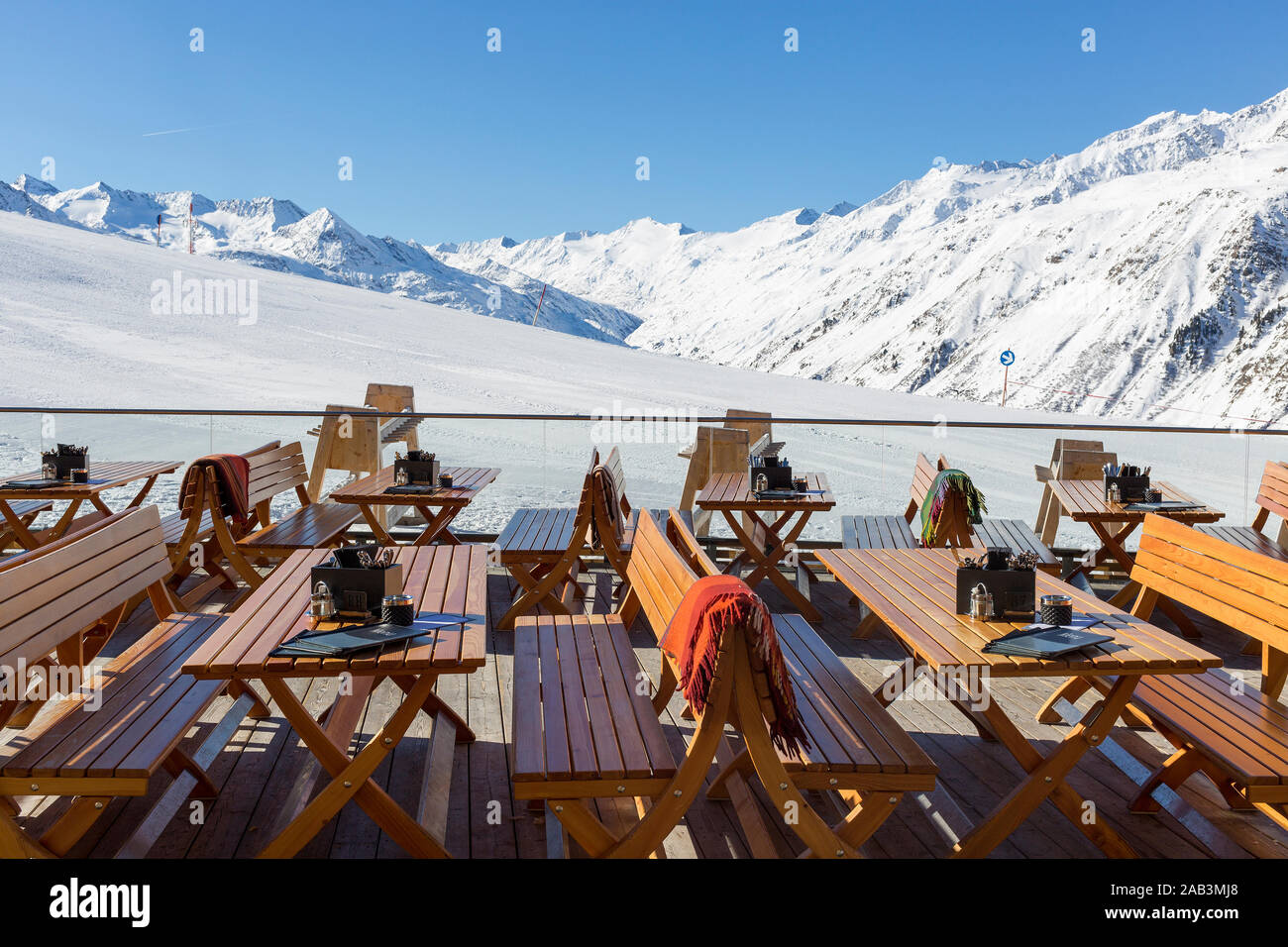 Stühle und Tische auf eine leere Terrasse an einem Ski cafe in einem österreichischen Resort mit schneebedeckten Bergen hinter Stockfoto