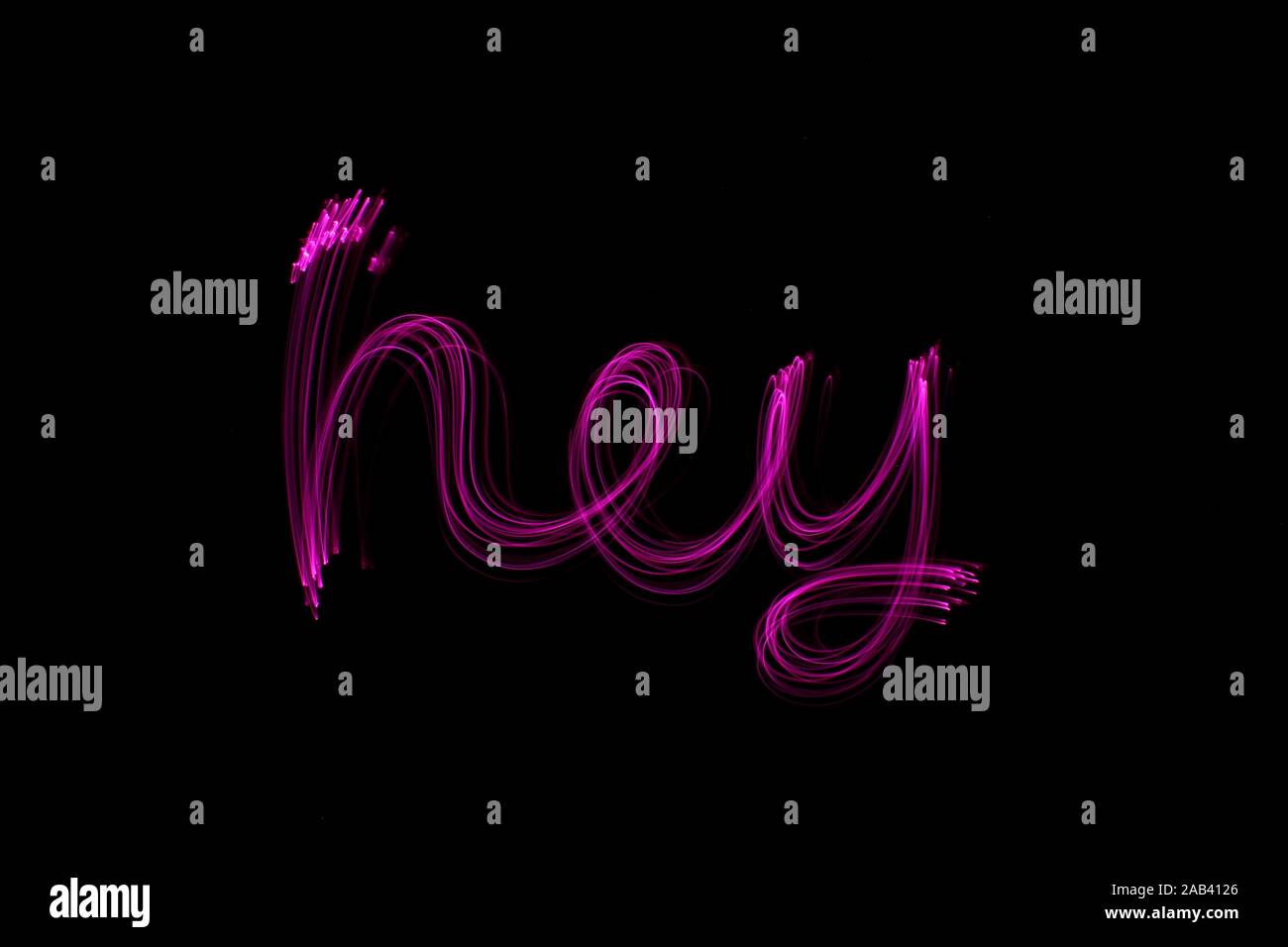 Lange Belichtung Foto des Wortes 'hey' in Rosa Neon Farbe in einer abstrakten Wirbeln, parallele Linien Muster vor einem schwarzen Hintergrund. Licht Malerei Stockfoto