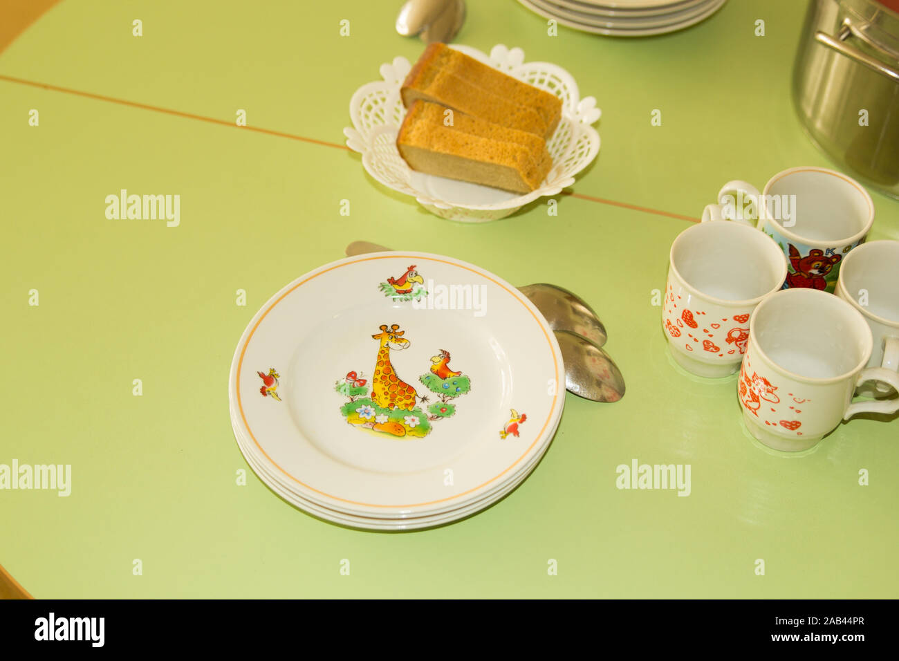 Serviert Esstisch für Kinder mit Brot, Teller mit Illustrationen. Farbenfroher Kindertisch. Kindergarten zur Mittagszeit. Stockfoto