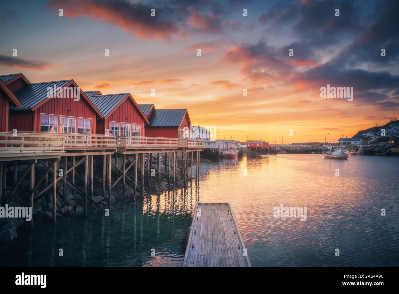 Red rorbu auf hölzernen Pfählen am Meer, kleinen Bootsanleger, bunte Himmel Stockfoto