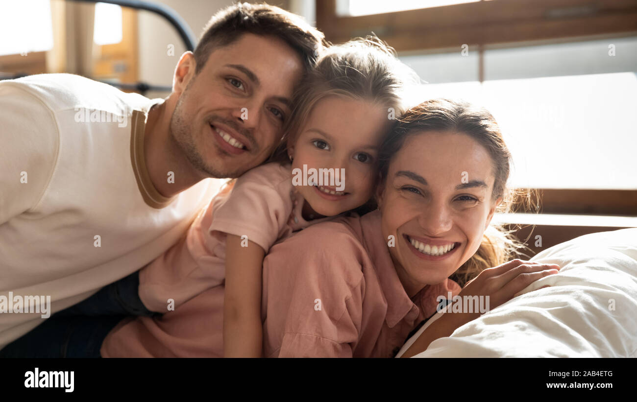 Glückliche Eltern und Kind Tochter an der Kamera auf der Suche nach Bett Stockfoto