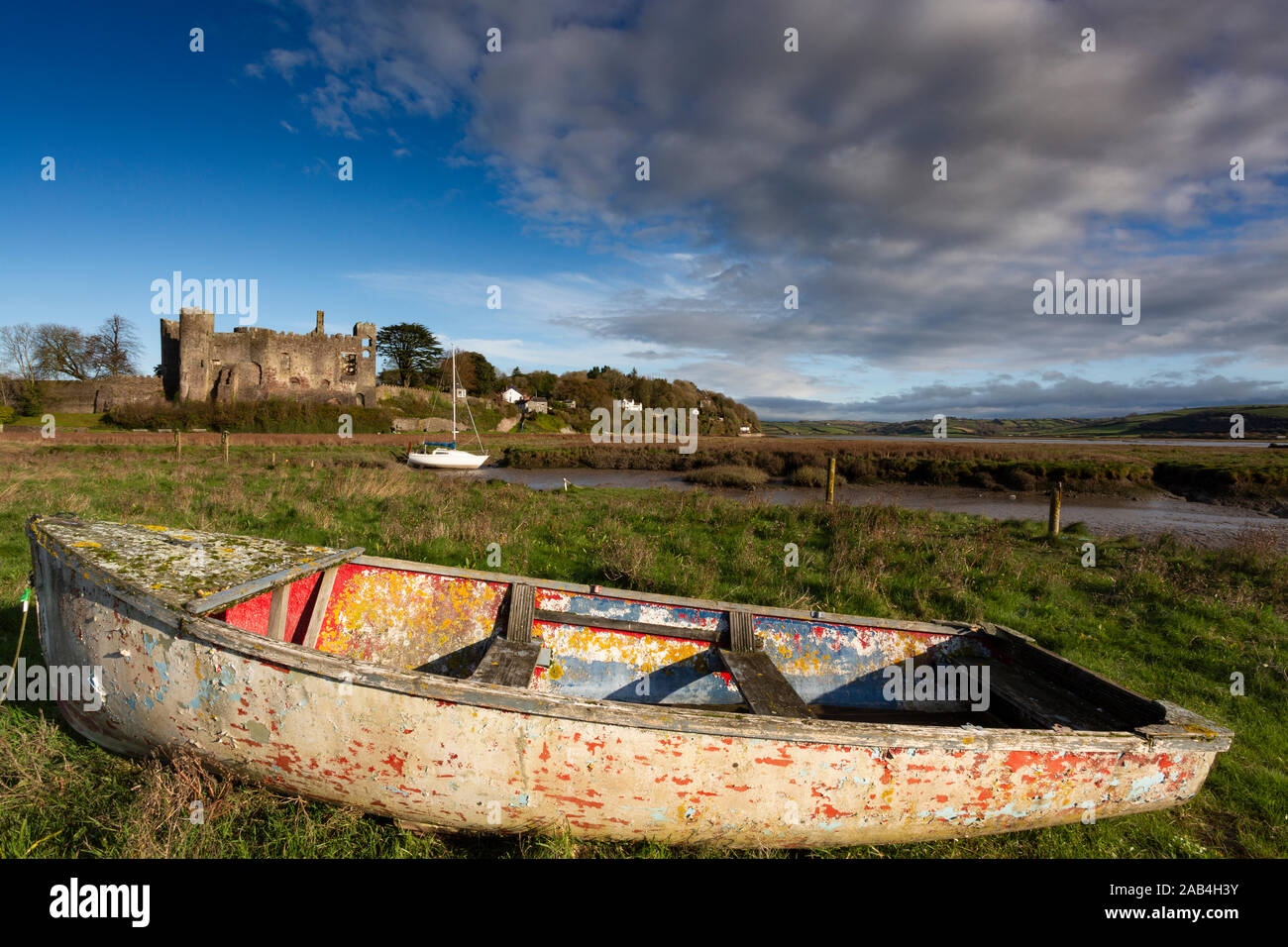 Laugharne Schloss in Carmarthenshire auf hellen Herbst Tag mit alten Ruderboot im Vordergrund Stockfoto