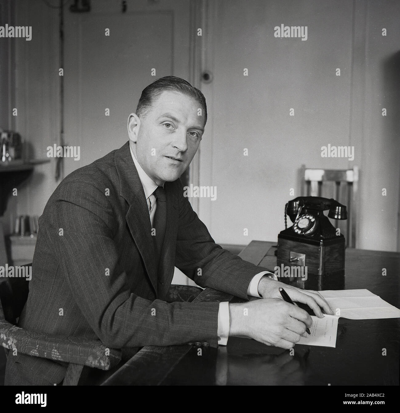 1950, historische, post-WW2 Großbritannien und ein Vorstand eines großen Industriellen Geschäft sitzt an seinem Schreibtisch in seinem Büro einen Brief schreiben, mit einem Telefon der Ära neben ihm, England, UK. Stockfoto