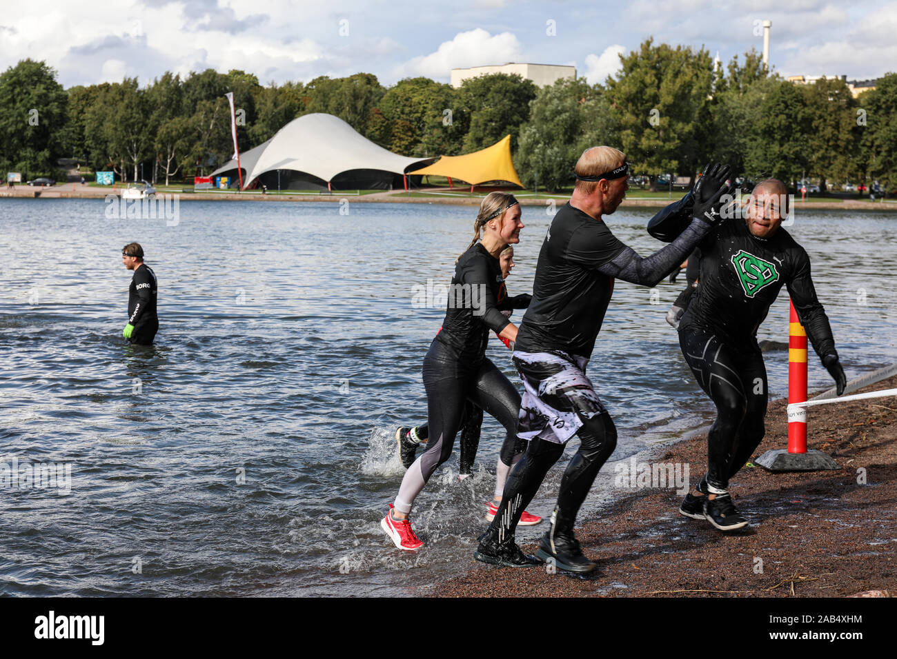 Obwohl Viking Hindernisparcours Rennen Teilnehmer, high-fiving nach Meer eintauchen in Helsinki, Finnland Stockfoto