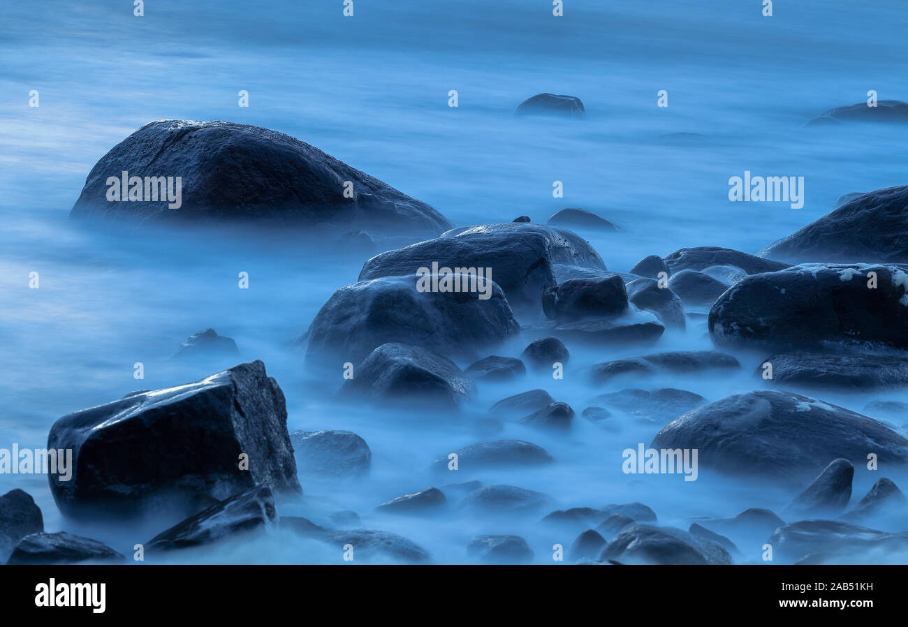 Steine im Wasser an einem kalten und windigen Sommer Nacht mit blauem Licht Stockfoto