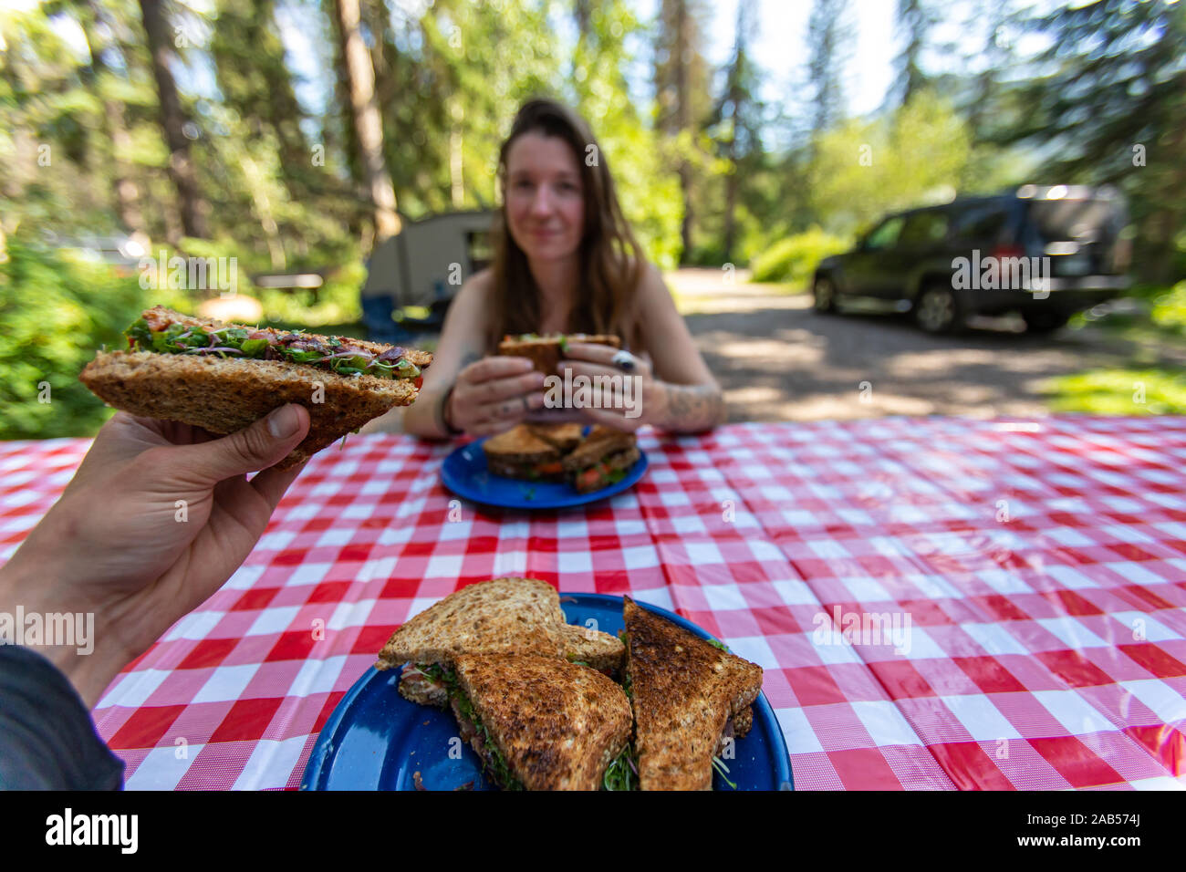 Selektiver Fokus von zwei erwachsenen Personen draußen sitzen an einem Picknicktisch in einem Natur Umwelt essen einige köstliche hausgemachte Sandwiches Stockfoto
