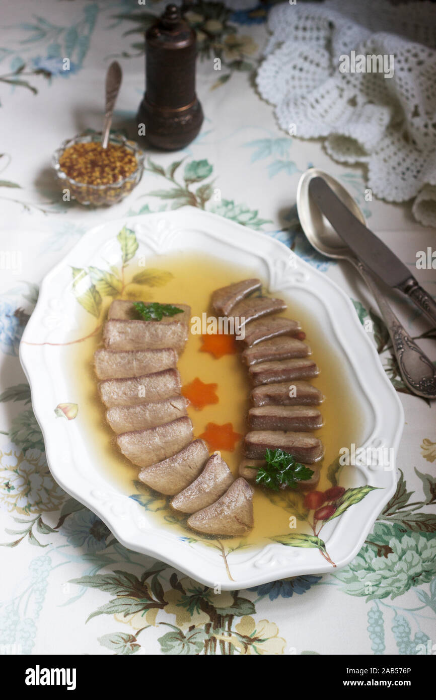 Aspic der Zunge verziert mit gekochten Karotten und Petersilie auf einem festlichen Hintergrund. Rustikaler Stil. Stockfoto