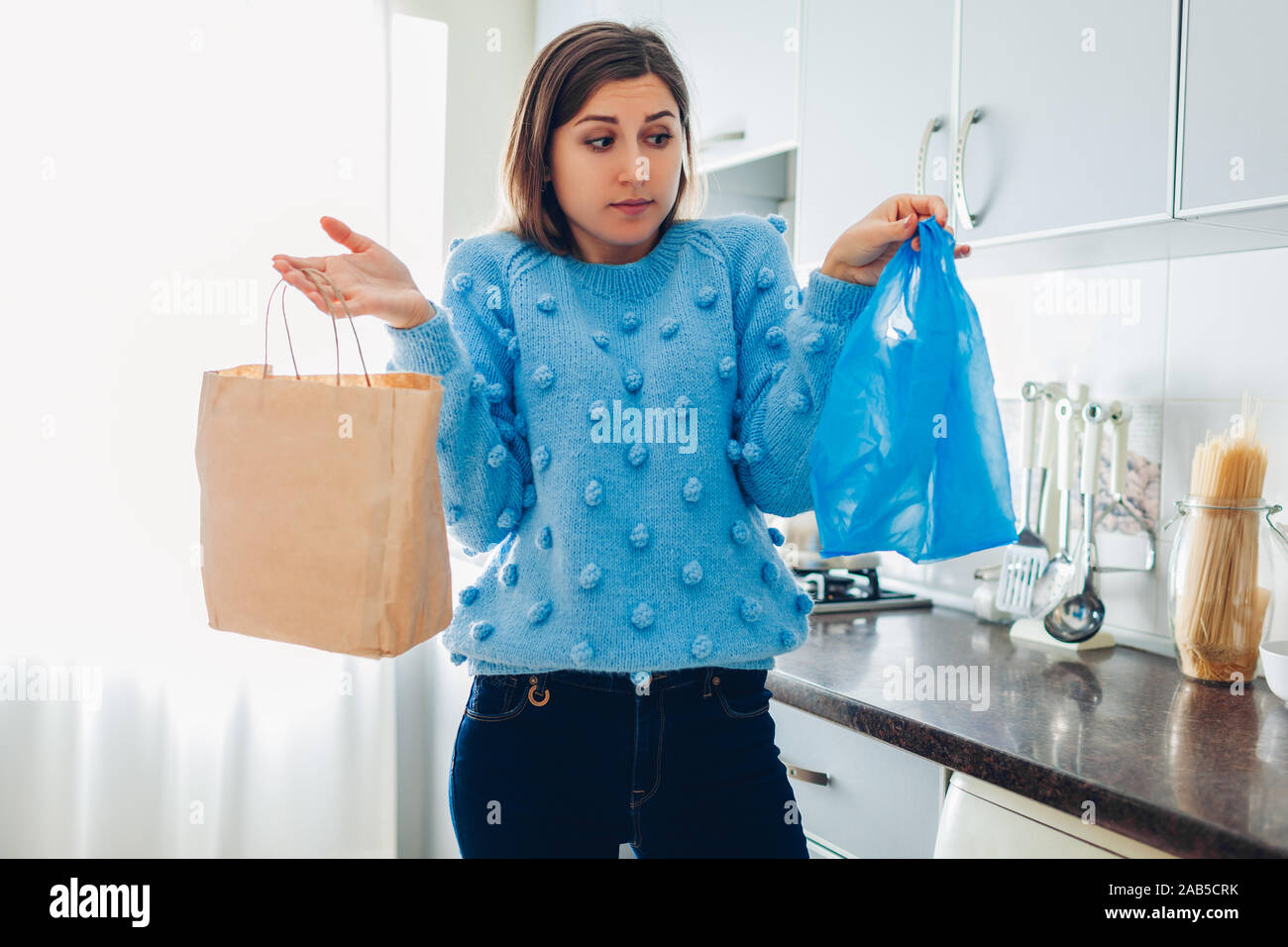 Plastik- oder papiertüte Wahl. Frau Wahl zwischen Eco und Polyethylen Paket auf Küche zu Hause Stockfoto