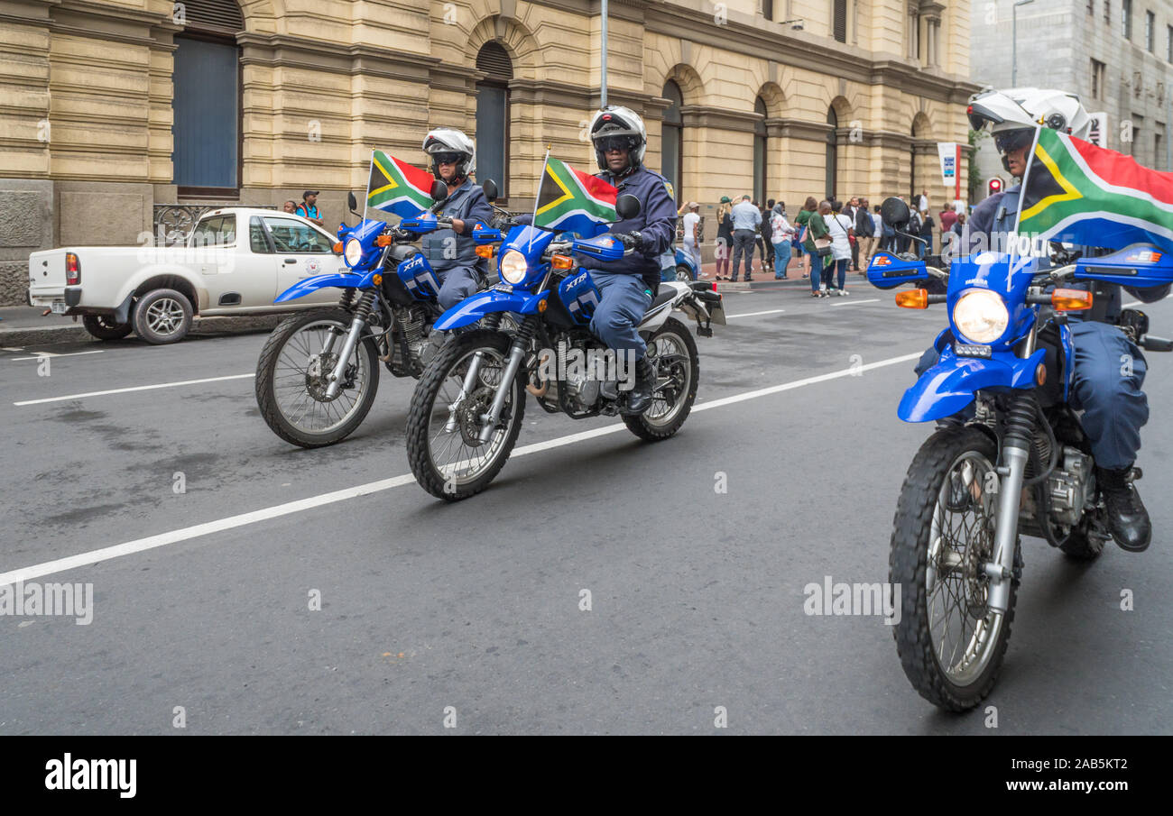 Die Südafrikanische Polizei auf Motorrädern oder Motorrädern Fahrt durch eine Stadt Straße in Kapstadt anzeigen Nationalflaggen der Springbock Sieg zu feiern. Stockfoto