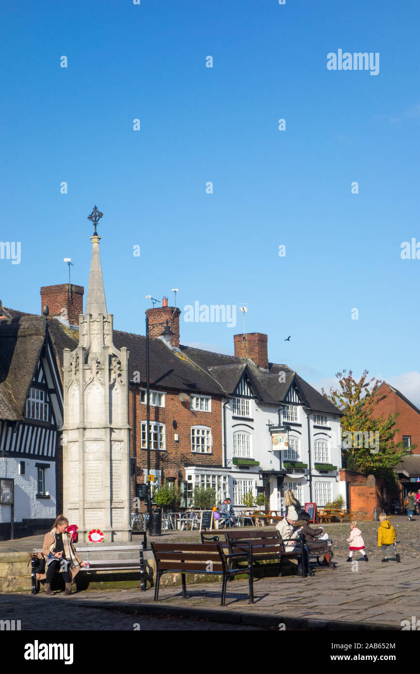 Menschen sitzen in den alten gepflasterten Marktplatz im Cheshire Marktstadt Sandbach Cheshire mit dem Kriegerdenkmal im Vordergrund. Stockfoto