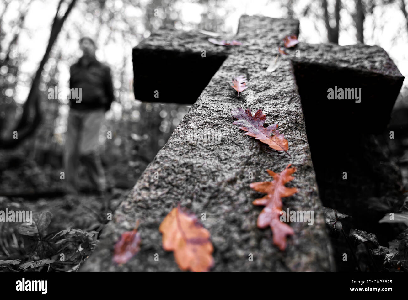 R.I.P. ein steinernes Kreuz fiel in einen Friedhof mit einem verschwommenen Mann auf der einen Seite und braune Blätter an der Oberseite Stockfoto