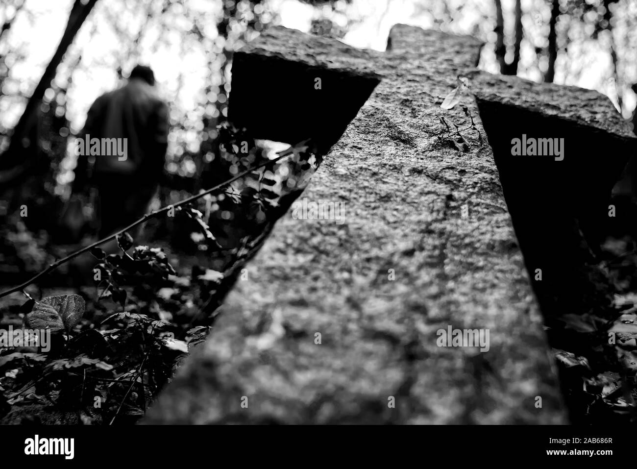 R.I.P. ein steinernes Kreuz fiel in einen Friedhof mit einem verschwommenen Mann an einer Seite Stockfoto