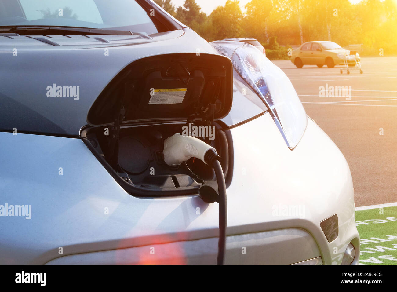 Umweltfreundliches Transportkonzept. Laden von Energie. Grau Auto ist auf Stromtankstelle in Parken berechnet. Sonnenlicht, сlose. Stockfoto