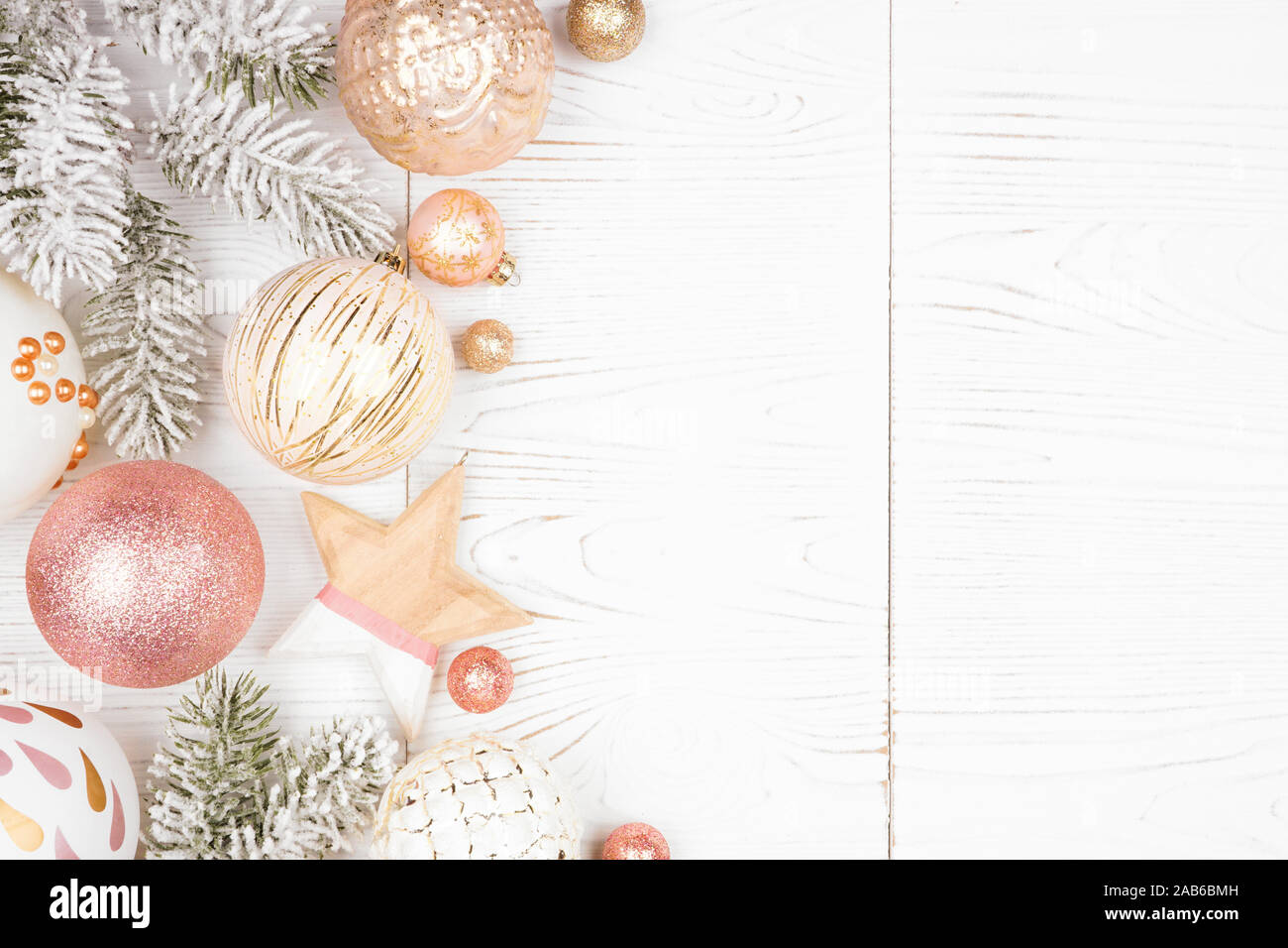 Weihnachten Seite Grenze der schneebedeckten Zweigen und Dusty Rose, Gold und Weiß Ornamente. Ansicht von oben auf einem weißen Holz Hintergrund. Stockfoto