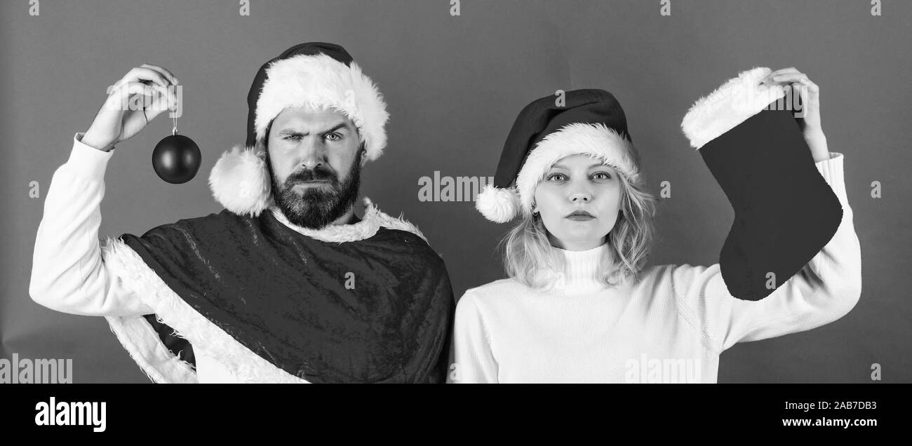 Weihnachtsfeier Konzept. Frau und bärtigen Mann in Santa Hut warten Weihnachten roten Hintergrund. Weihnachtsstrumpf Tradition. Paar weihnachten santa Kostüm halten Socke und Ornament Kugel. Stockfoto