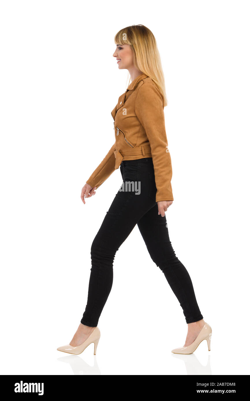 Schöne junge Frau in Braun Leder Jacke, schwarze Jeans und High Heels ist  Wandern und Wegsehen. Von der Seite. Volle Länge studio shot Isolat  Stockfotografie - Alamy