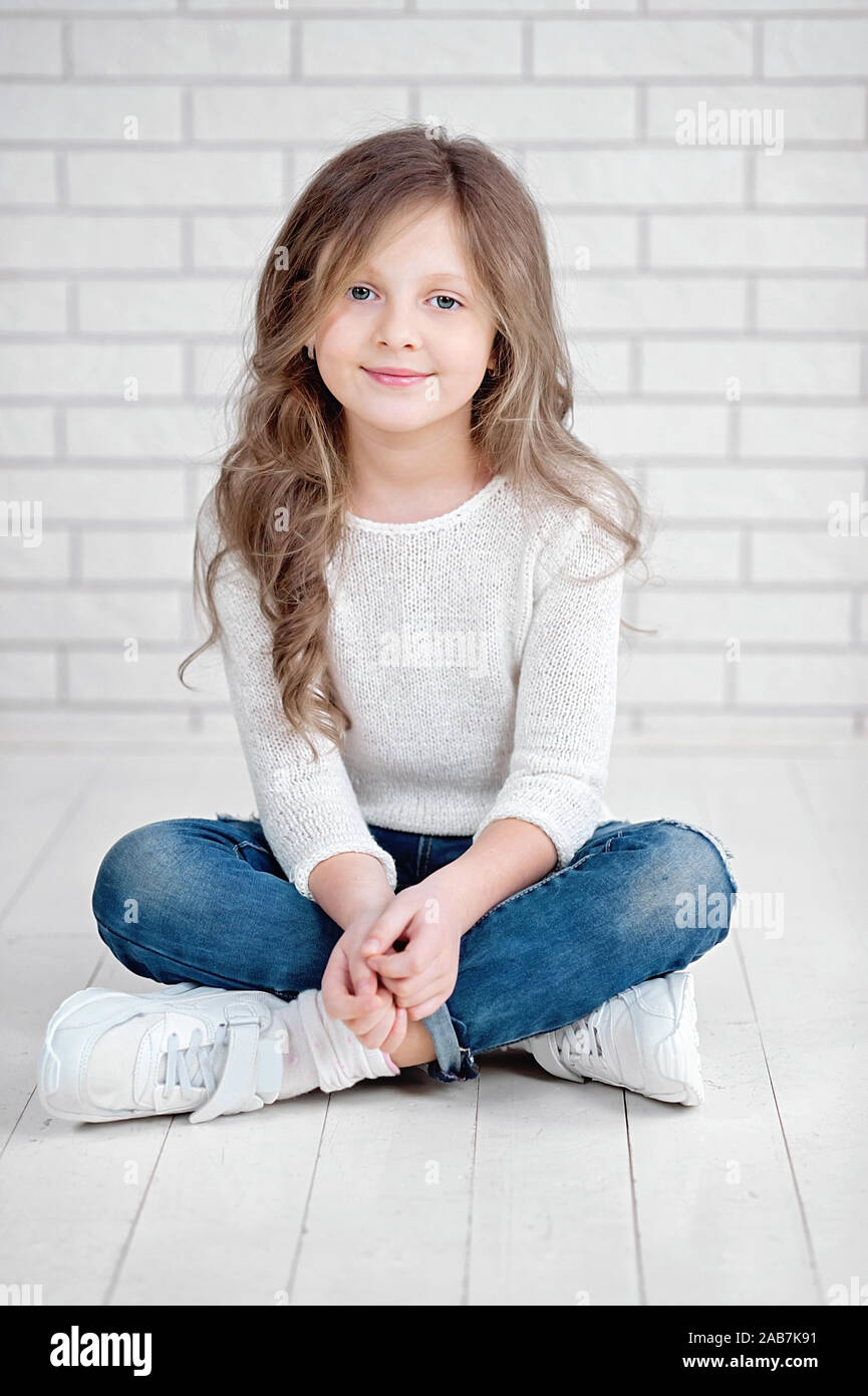 Portrait von niedlichen kleinen 7 Jahre alten Mädchen lächelnd und sitzen auf weißem Holzfußboden im Studio. Stockfoto