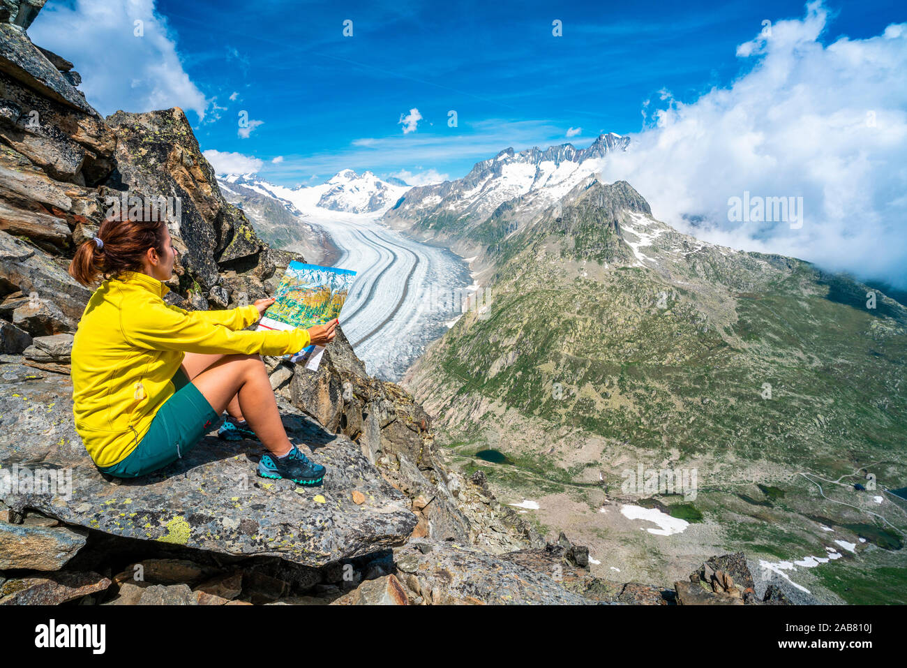 Frau suchen an der Karte sitzen auf den Felsen am Eggishorn Aussichtspunkt über Aletschgletscher, Berner Alpen, im Kanton Wallis, Schweiz, Europa Stockfoto