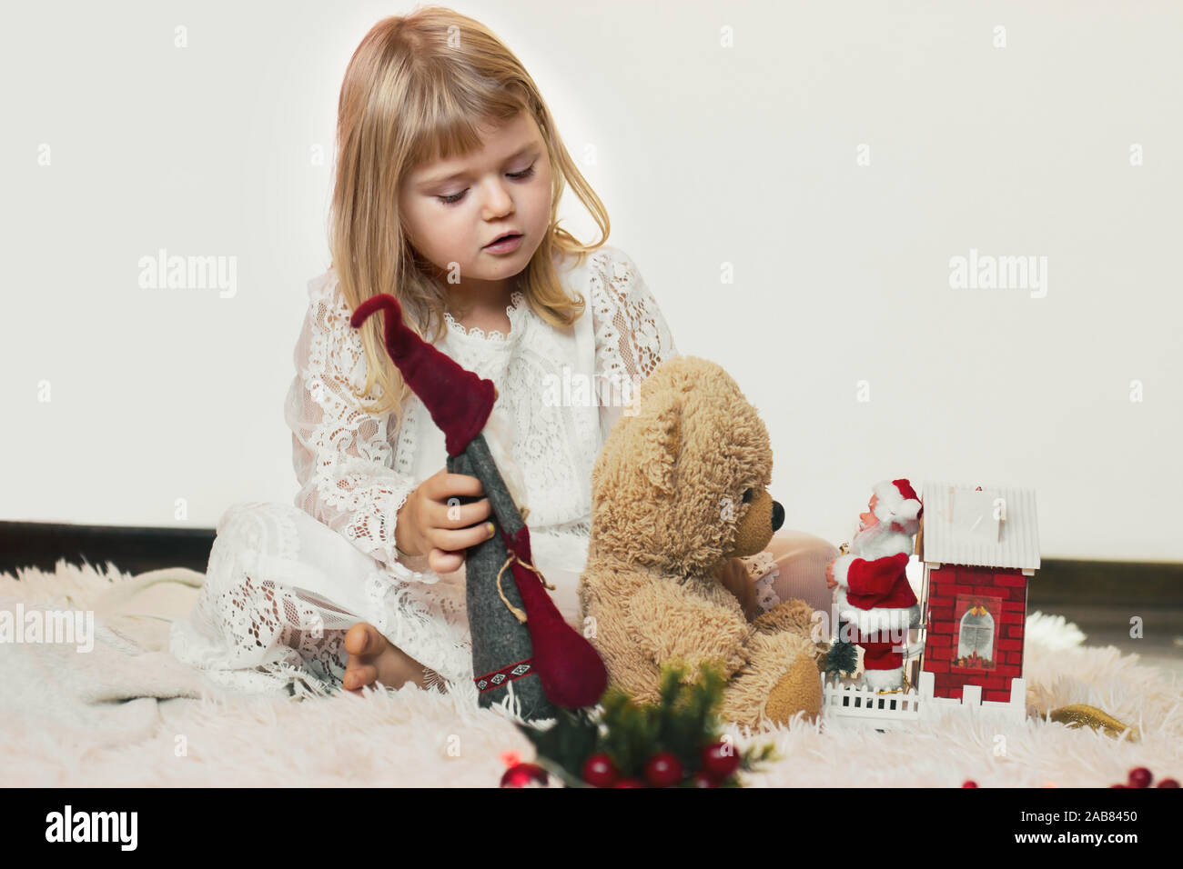 Süße kleine blonde Mädchen sitzen auf dem Boden und spielen mit ihren Teddybären und Little Santa Claus Weihnachten Spielzeug Stockfoto