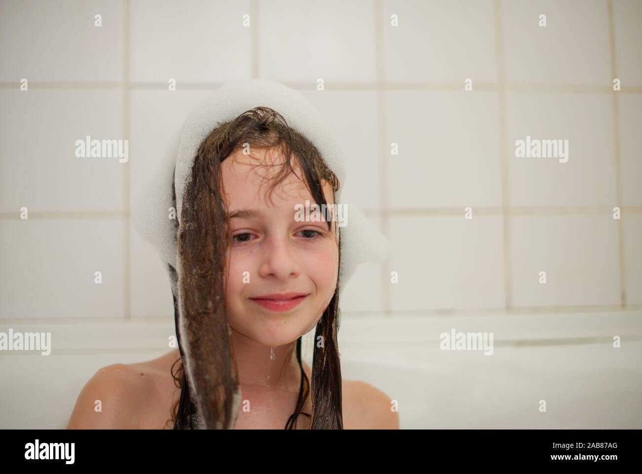 Junge Mädchen in der Badewanne. Ein kleines Mädchen taucht in der Badewanne mit Schaum. Ein Mädchen von 9 Jahren nimmt eine Badewanne. Reinheit Konzept Stockfoto