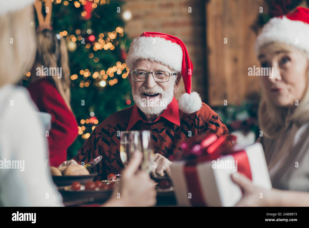 Phot von Großvater positive fröhlich lächelnd in Brillen Brillen Tragen santa hut Kopfbedeckung Gefühl festliche Stimmung im Gespräch mit Gästen Stockfoto