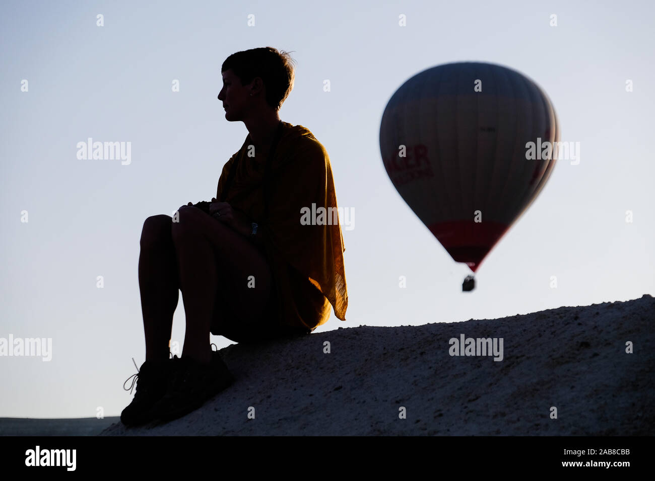 Die Frau setzte sich auf einen Felsen mit dem Heißluftballon in der Entfernung Stockfoto