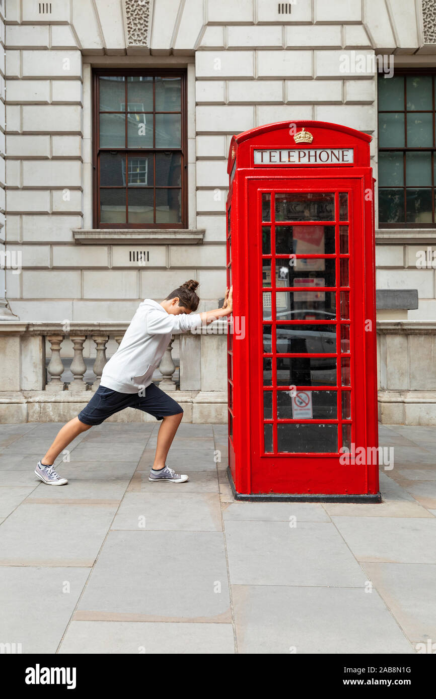 Junge drückt eine rote Telefonzelle in London. Ansicht von vorn Stockfoto